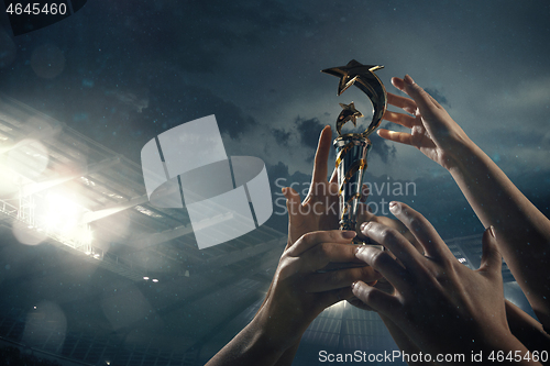 Image of Award of victory, male hands tightening the cup of winners against cloudy dark sky