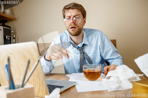 Image of Sick man while working in office, businessman caught cold, seasonal flu.