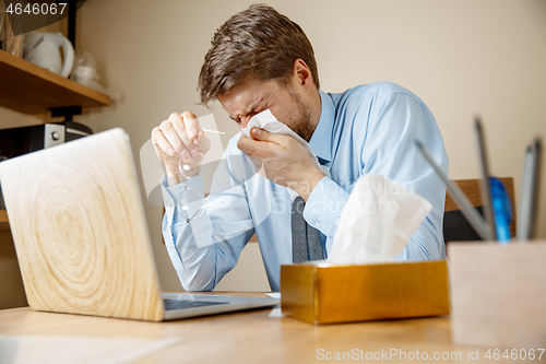 Image of Sick man while working in office, businessman caught cold, seasonal flu.