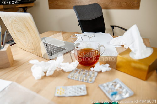 Image of A cup of tea with pills, medicines, paper handkerchiefs at desk