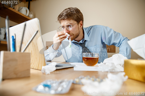 Image of Sick man while working in office, businessman caught cold, seasonal flu.