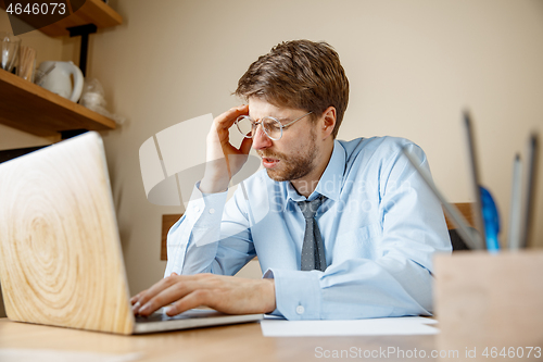 Image of Feeling sick and tired. Frustrated young man massaging his head while sitting at his working place in office