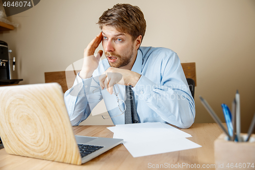 Image of Feeling sick and tired. Frustrated young man massaging his head while sitting at his working place in office