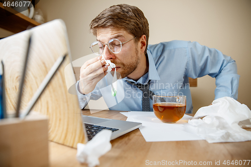 Image of Sick man while working in office, businessman caught cold, seasonal flu.