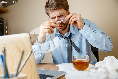 Image of Sick man while working in office, businessman caught cold, seasonal flu.