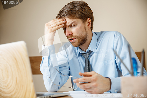 Image of Feeling sick and tired. Frustrated young man massaging his head while sitting at his working place in office