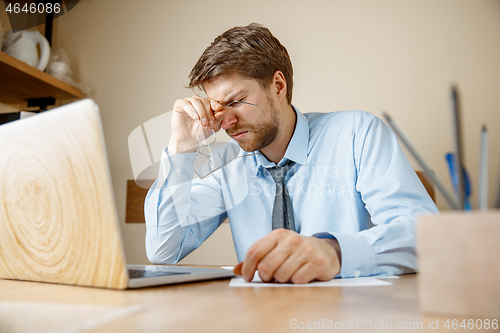 Image of Feeling sick and tired. Frustrated young man massaging his head while sitting at his working place in office