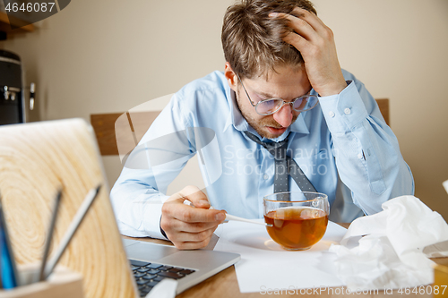 Image of Feeling sick and tired. Frustrated young man massaging his head while sitting at his working place in office