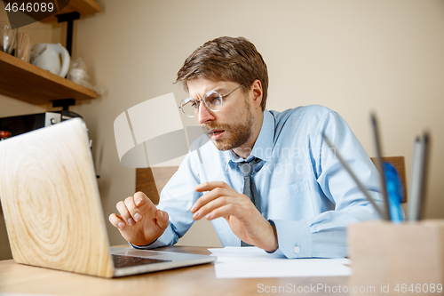 Image of Feeling sick and tired. Frustrated young man massaging his head while sitting at his working place in office