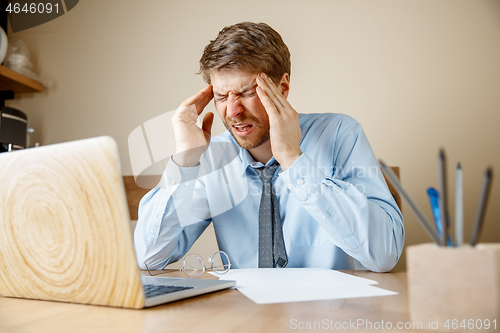 Image of Feeling sick and tired. Frustrated young man massaging his head while sitting at his working place in office