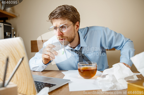 Image of Sick man while working in office, businessman caught cold, seasonal flu.