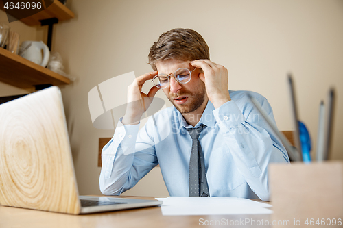 Image of Feeling sick and tired. Frustrated young man massaging his head while sitting at his working place in office