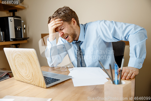 Image of Feeling sick and tired. Frustrated young man massaging his head while sitting at his working place in office