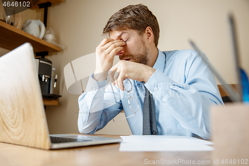 Image of Feeling sick and tired. Frustrated young man massaging his head while sitting at his working place in office