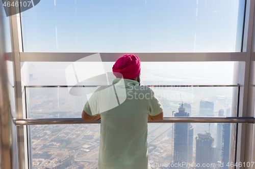 Image of Indian sikh man wearing traditional colorfu turban, admiring city view from modern observing platform at top of the tallest skyscraper in the world, Burj Khalifa in Dubai, UAE.