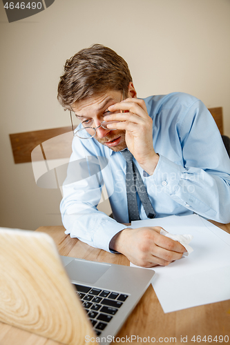 Image of Feeling sick and tired. Frustrated young man massaging his head while sitting at his working place in office