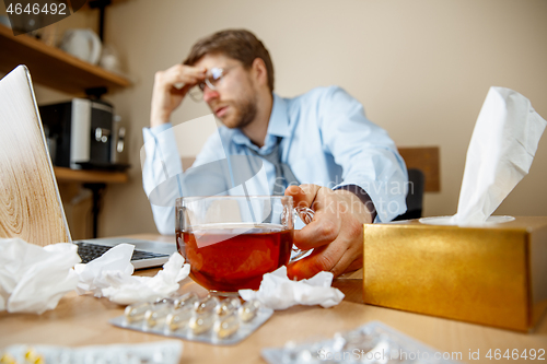 Image of Feeling sick and tired. Frustrated young man massaging his head while sitting at his working place in office