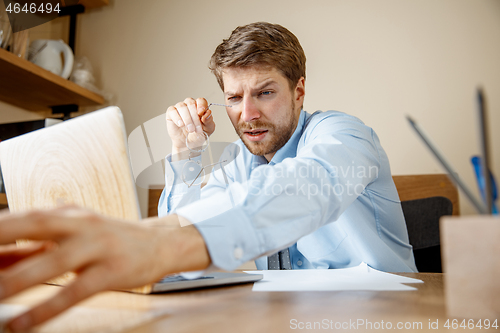 Image of Feeling sick and tired. Frustrated young man massaging his head while sitting at his working place in office