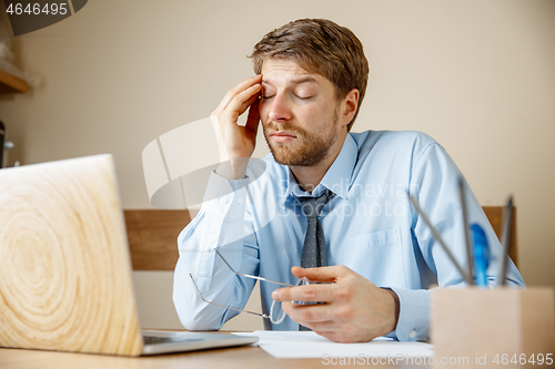 Image of Feeling sick and tired. Frustrated young man massaging his head while sitting at his working place in office