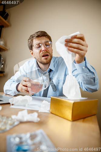 Image of Sick man while working in office, businessman caught cold, seasonal flu.