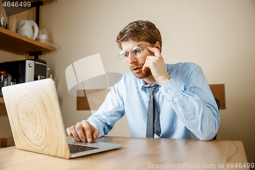 Image of Feeling sick and tired. Frustrated young man massaging his head while sitting at his working place in office