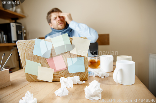 Image of Feeling sick and tired. Frustrated young man massaging his head while sitting at his working place in office