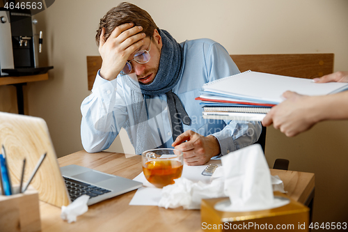 Image of Feeling sick and tired. Frustrated young man massaging his head while sitting at his working place in office