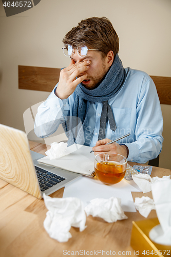 Image of Feeling sick and tired. Frustrated young man massaging his head while sitting at his working place in office