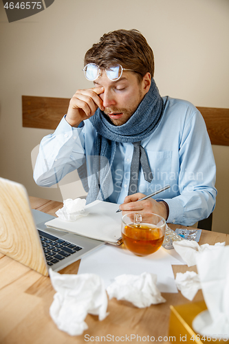 Image of Feeling sick and tired. Frustrated young man massaging his head while sitting at his working place in office