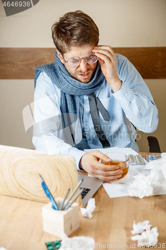 Image of Feeling sick and tired. Frustrated young man massaging his head while sitting at his working place in office