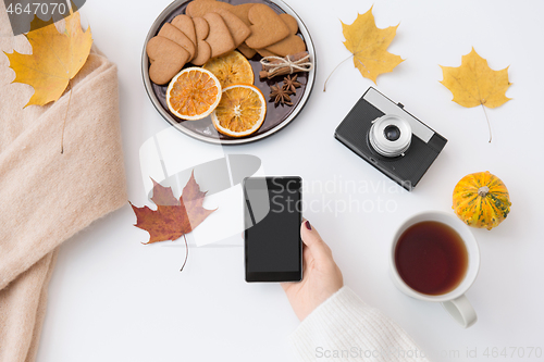 Image of hand with smartphone, tea and autumn leaves