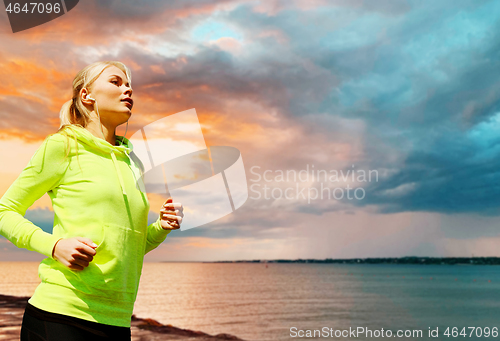 Image of woman with earphones running over sea sunset