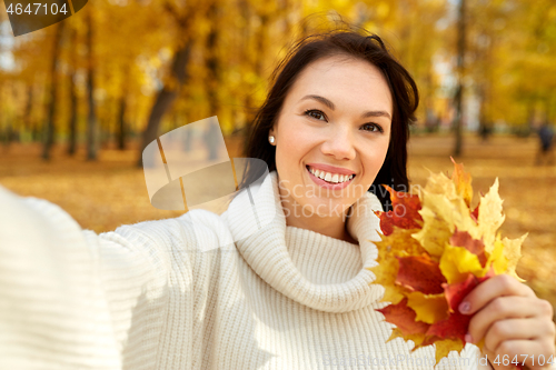 Image of woman with leaves taking selfie in autumn park