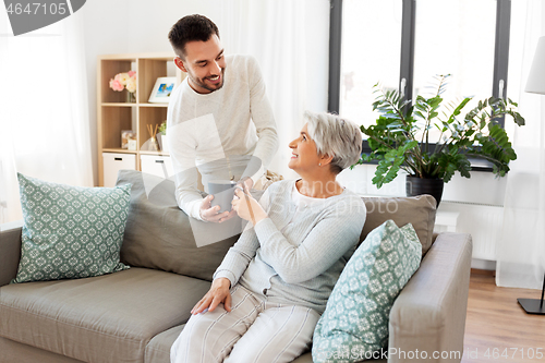 Image of adult son bringing coffee to senior mother at home