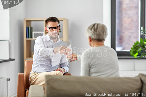 Image of psychologist giving glass of water to senior woman