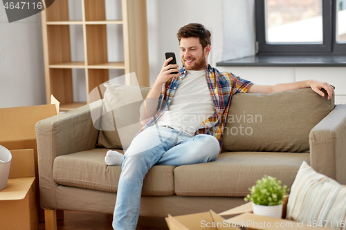 Image of man with smartphone and boxes on sofa at new home