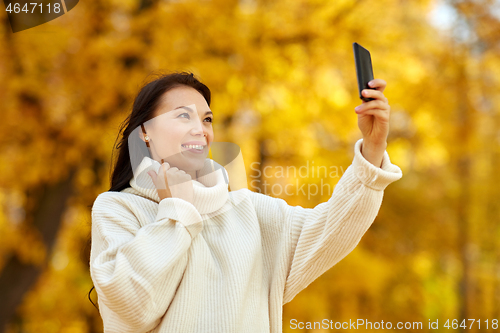 Image of woman taking selfie by smartphone at autumn park