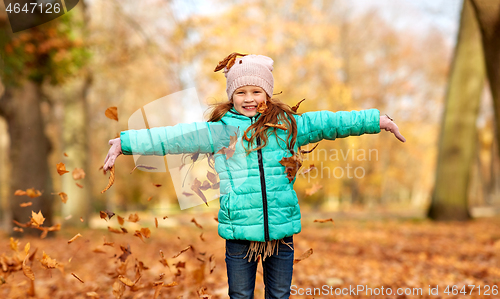 Image of happy girl playing with leaves at autumn park