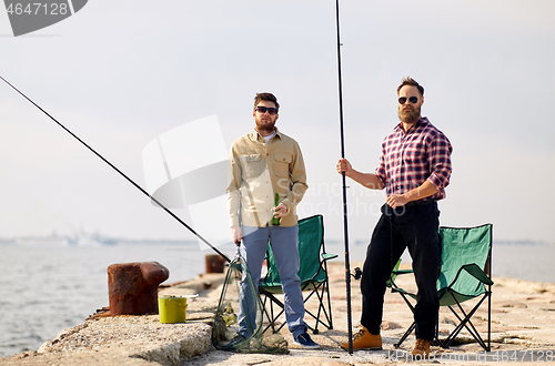 Image of happy friends with fishing rods and beer on pier