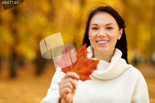 Image of happy young woman with maple leaf in autumn park