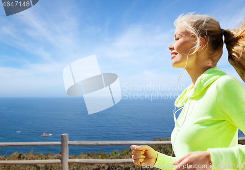 Image of woman with earphones running at seaside