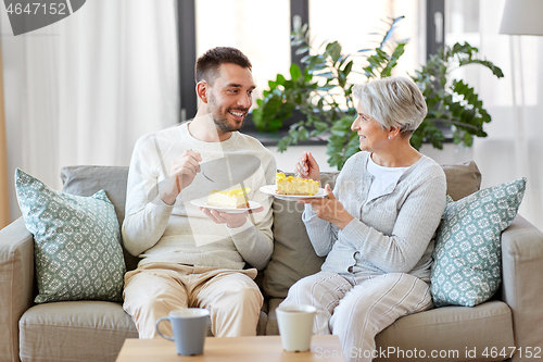 Image of senior mother and adult son eating cake at home