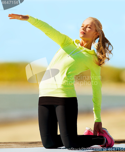 Image of woman stretching on exercise mat on beach