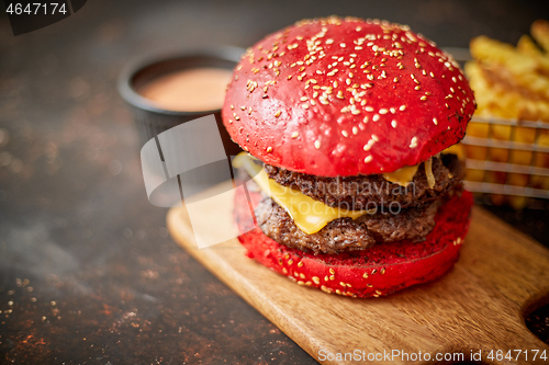 Image of Homemade red sesame bun double bacon cheese burger. Served with french fries on wooden board.