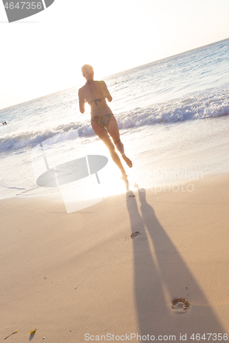 Image of Woman running on the beach in sunset.