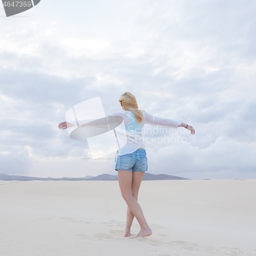 Image of Carefree woman enjoying freedom on white sand dune at dusk.