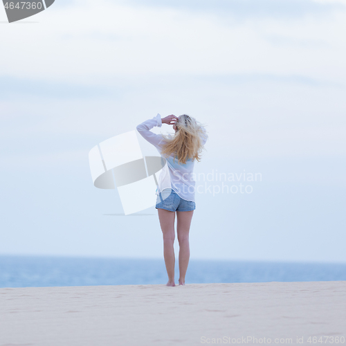 Image of Woman on sandy beach in white shirt at dusk.