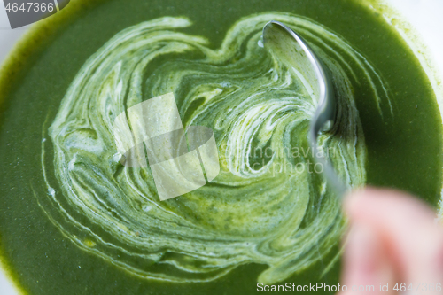 Image of Creamy spinach soup in plate beeing mixed with spoon