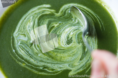 Image of Creamy spinach soup in plate beeing mixed with spoon