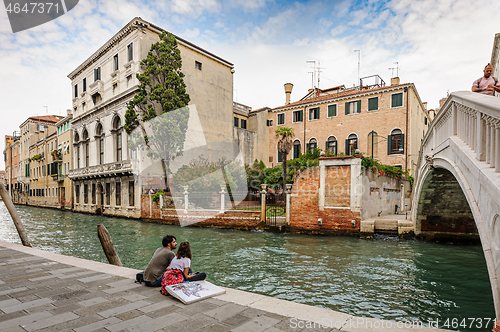 Image of Venice, Italy. Romainic couple sitting at canal\'s sidewalk close to bridge in historic part of the city